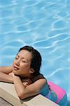 Woman leaning at the edge of swimming pool, arms crossed, eyes closed, high angle view