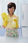 Woman in kitchen, holding cleaning detergent and sponge