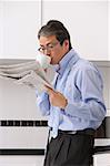 Man in kitchen getting ready for work, drinking coffee and reading newspaper, tie loose around neck