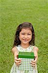 Girl standing on grass, holding gift box towards camera