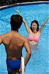 Woman in swimming pool, arms outstretched, looking at man standing in front of her