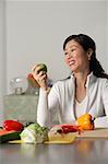 Femme dans la cuisine, à la recherche chez apple, légumes sur une table autour d'elle