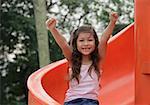 Girl coming down playground slide arms outstretched, smiling at camera
