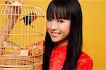 Young woman holding lovebird in bird cage, smiling