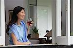 Woman at home, looking out of the window, holding wine glass