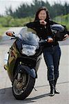 Mature woman leaning against motorcycle, holding helmet