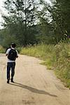 Man walking down dirt road, hiking, back to camera