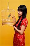 Young woman holding lovebird in bird cage, looking at bird