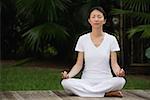 Woman in tropical setting, meditating on porch, eyes closed, in yoga OM posture.