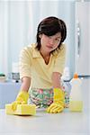 Woman in kitchen wearing gloves, cleaning kitchen counter with sponge