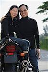 Mature couple looking at camera, woman sitting on motorcycle