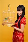 Young woman holding lovebird in bird cage, smiling