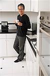 Man in kitchen, leaning on counter, holding coffee cup and smiling at camera