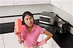 woman standing in kitchen, wearing gloves and apron for cleaning, holding sponge and thinking.