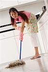 woman mopping floors of kitchen, wearing gloves and apron