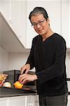 Man in kitchen cutting lemon, looking at camera and smiling