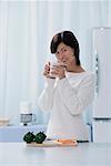 Femme dans la cuisine, tenant une tasse, en regardant la caméra