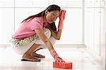 Woman cleaning kitchen floor with big pink sponge, tired