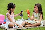 Two girls sitting on picnic blanket, playing with dolls