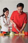 Couple in kitchen, man cutting vegetables, woman watching him