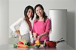 Mother and adult daughter in kitchen preparing a meal, looking at camera