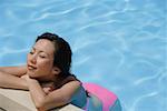 Woman with eyes closed, leaning on the edge of swimming pool