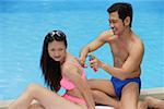 Couple by swimming pool, man applying sun tan lotion on woman