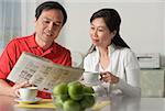 Mature couple at home, looking at newspaper and having coffee