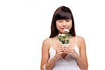 Junge Frau trägt weißes Kleid, holding kleine Pflanze und Blume riechen