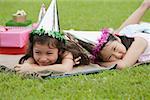 Two girls wearing party hats lying on picnic blanket, resting