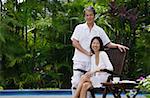 Couple relaxing outdoors by swimming pool, looking at camera, portrait