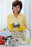 Woman in kitchen, cleaning pots and pans, smiling at camera