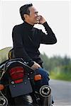 Mature man leaning on motorcycle, talking on mobile phone