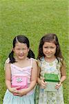 Two girls with gift boxes, standing side by side, smiling at camera