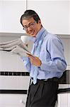 Man in kitchen getting ready for work, drinking coffee and reading newspaper, smiling at camera with tie loose around neck