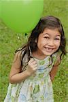 Girl holding green balloon, smiling at camera