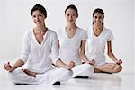 three women of mixed race sitting in yoga posture OM, meditating, looking at camera, smiling