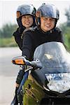 Man and woman riding motorcycle, wearing helmets, looking at camera