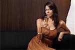 Woman sitting on couch, holding champagne glass, smiling at camera