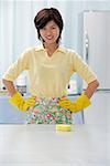 Woman in kitchen, wearing gloves and apron, hands on hips