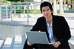 A man uses his laptop outdoors while he looks at the camera