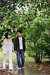 A young couple hold hands and stroll down a garden path together
