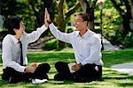 Two men eat their lunch together in the park and high five