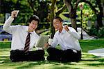 Two men get excited as they read the newspaper in the park