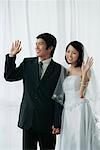 A newlywed couple hold hands and wave