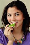 Ein junges Mädchen schaut die Kamera, wie sie ein Stück Obst isst