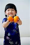 A small girl holds out two mandarin oranges