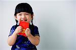 Une petite fille détient un paquet rouge qu'elle regarde la caméra
