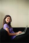 A teenage girl smiles at the camera as she uses a laptop