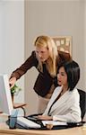 Two woman look at a computer while at work